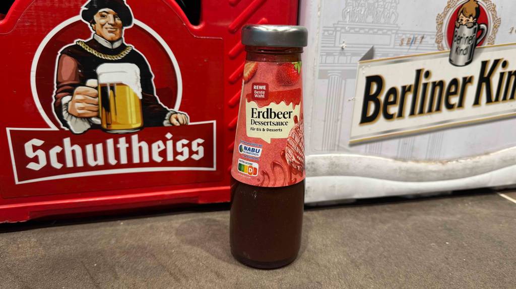 Eine Flasche der getesteten Erdbeersauce worauf der Nutriscore diese Sauce mit einem D bewertet hat, steht vor Bierkisten.