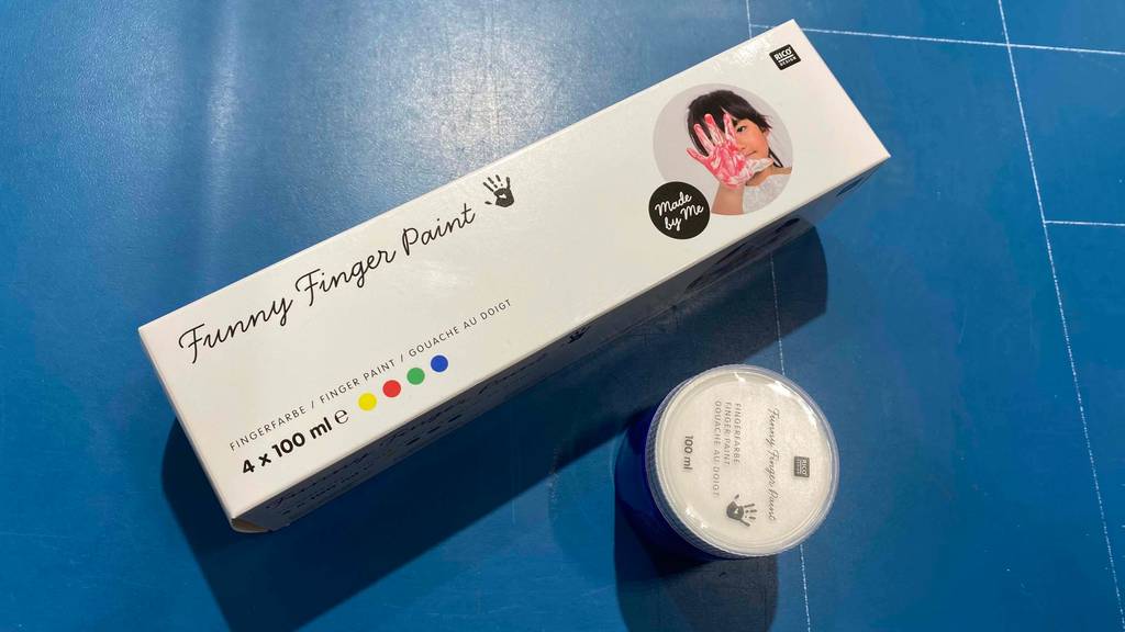 Fingerfarben im Test: Verpackung Fingerfarben liegt neben einem blauen Fingerfarben-Döschen.