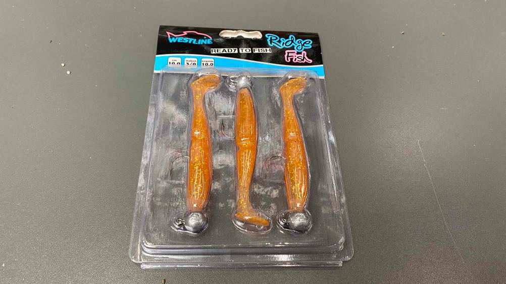 Getestete Gummifische in ihrer Verpackung auf einer grauen Fläche liegend.
