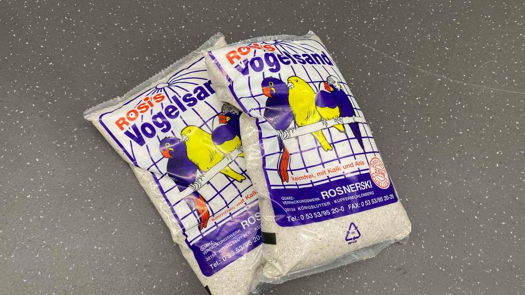 Vogelsand-Test: zwei Packungen Vogelsand liegen auf einem Boden übereinander. 