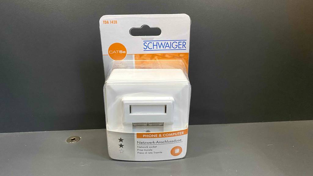 Netzwerkdose-Test: eine Netzwerkdose in der Verpackung vor grauem Hintergrund platziert. 