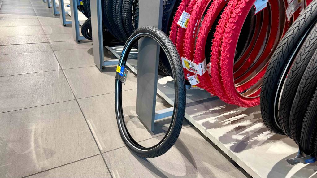 Fahrradreifen 26 Zoll-Test: Ein schwarzer Reifen steht vor einem Verkaufsstand mit roten Reifen.