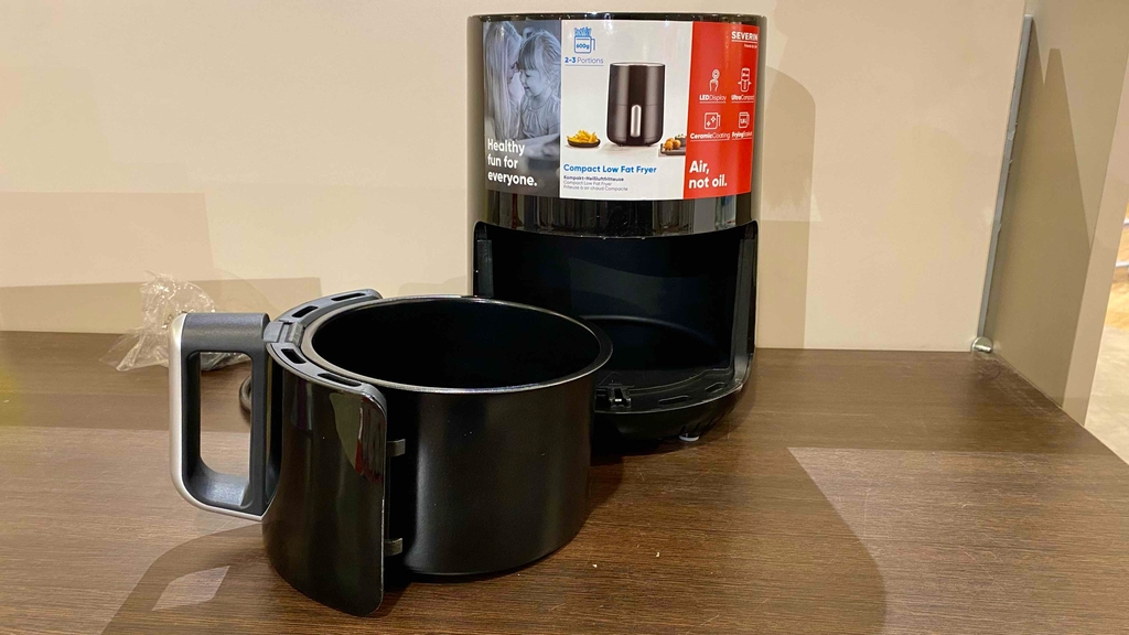 Im Test: Eine kleine Heißluftfritteuse mit offenem Fach vor einer hellen Wand.