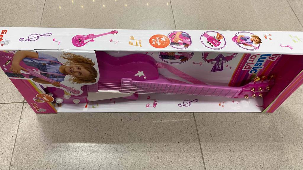 Im Karton inklusive Mädchen-Bild, verpackte, rosa Kindergitarre im Test. Auf der Seite stehend.
