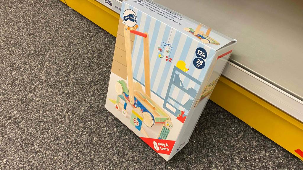 Lauflernwagen aus Holz getestet: Ein verpackter Wagen von schräg oben lehnt an einem Regalboden.