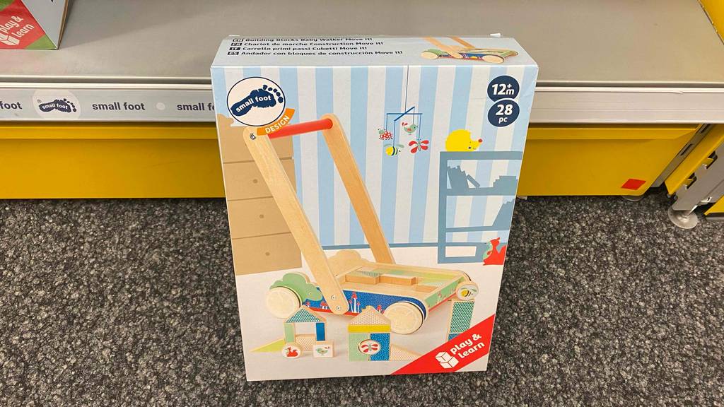 Ein getesteter Lauflernwagen aus Holz originalverpackt lehnt an einem gelben Sockel.