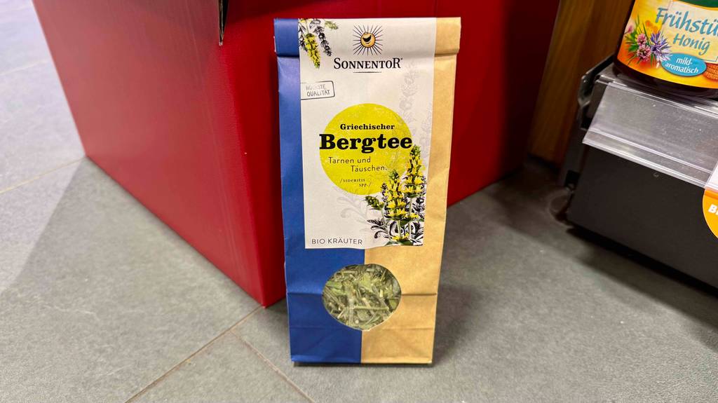 Ein Beutel des getesteten griechischen Bergtees steht auf dem Boden vor einem Regal.