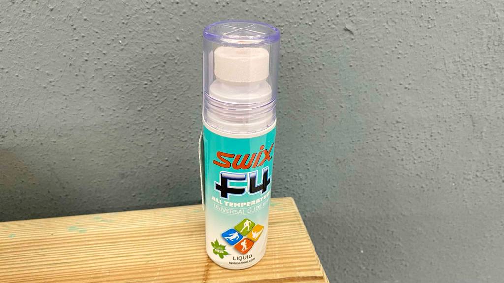 Skiwachs im Test: eine Flasche Skiwachs vor einer grauen Wand stehend.