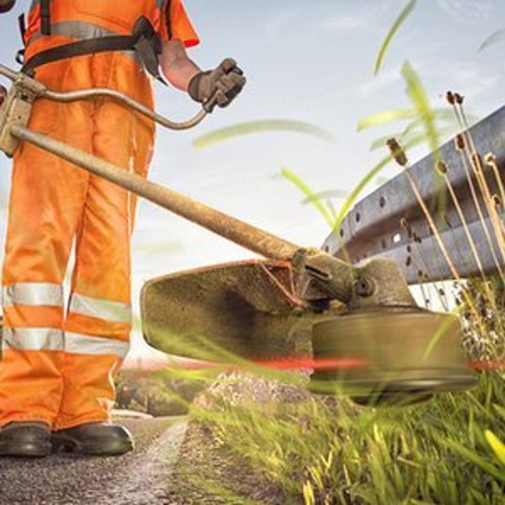 Arbeiter, der mithilfe einer 4-Takt-Motorsense mit Fadenspule Fahrbahnrand mäht