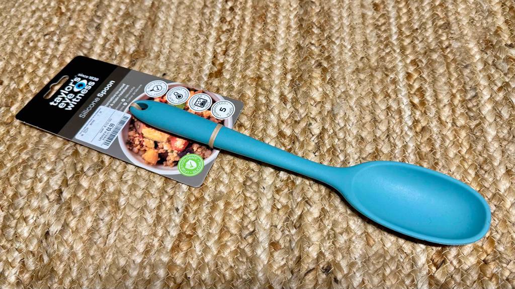 Ein blauer getesteter Silikon-Kochlöffel liegt auf einem Teppich.