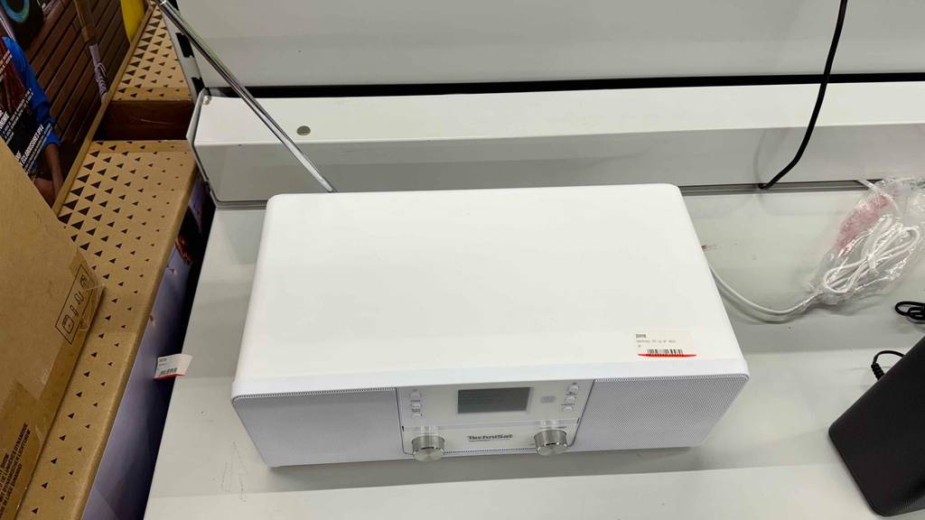 Ansicht von oben auf einen weißen getesteten Radiowecker mit CD-Player und Antenne, der auf einem Ausstellungsregal steht.