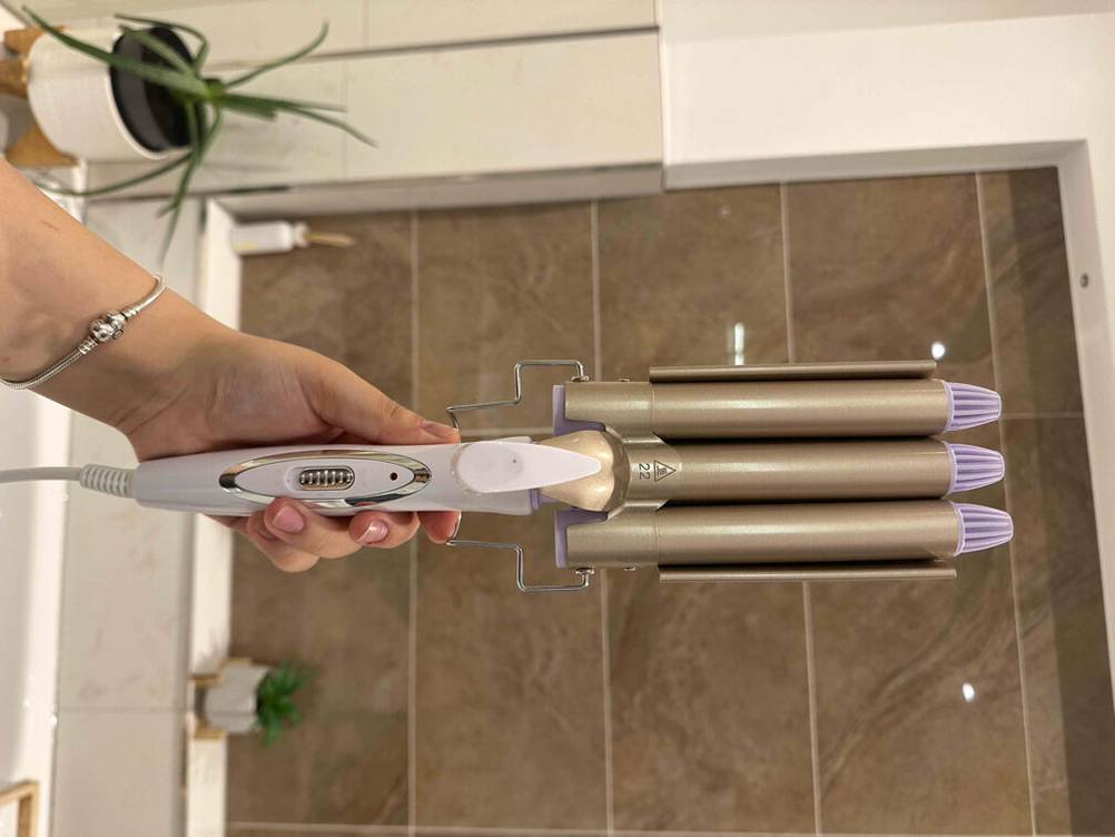 Der getestete Lockenstab-mit-3-Stäben wird in einem Badezimmer in der Hand gehalten.
