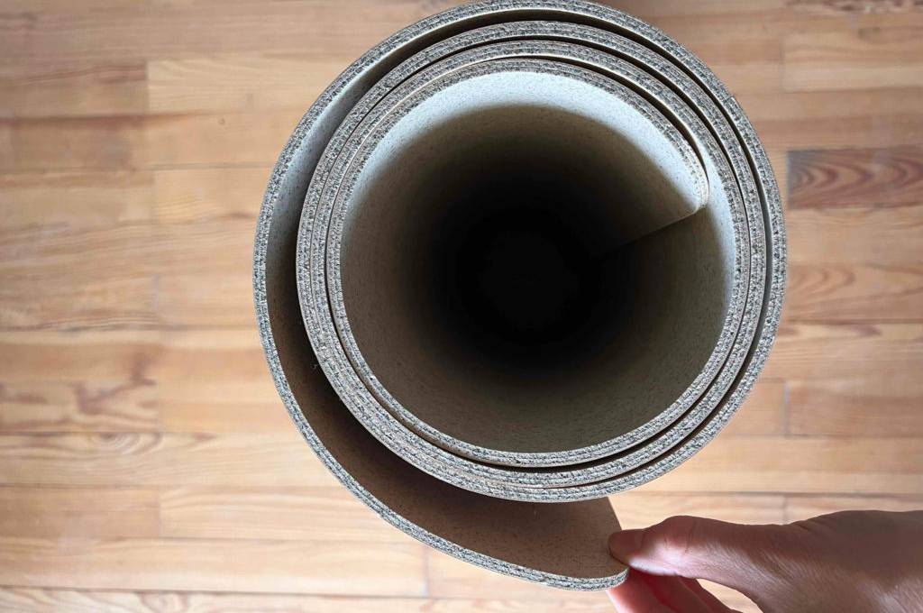 Eine getestete Yogamatte auf Kork, eingerollt von oben auf einem Holzboden.