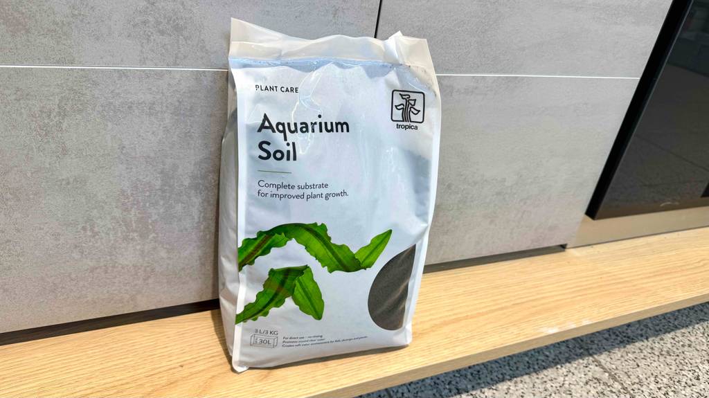 Im Test: Der Aquarium-Bodengrund in der weißen Kunststofftüte für 30 Liter steht vor einer gefliesten Wand.