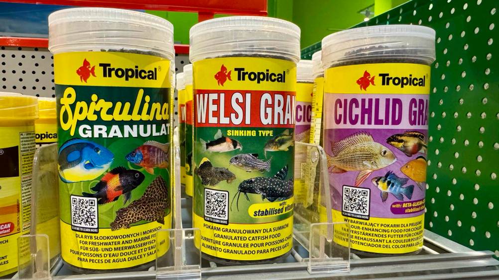 Das getestete Welsfutter steht neben Spirulina-Granulat in einem Regal.