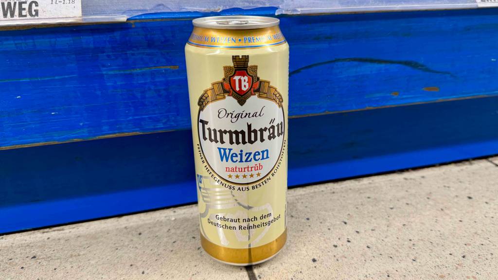 Eine getestete Dose Weizenbier steht auf einem Boden vor einem Regal.