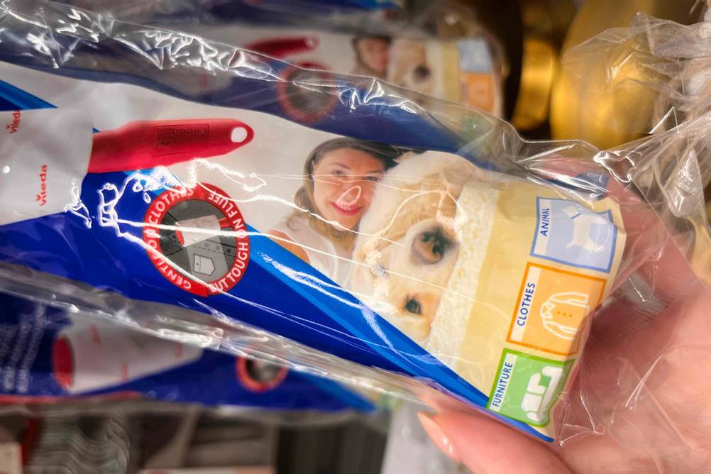 Tierhaarentferner getestet: Eine Hand hält einen verpackten Tierhaarentferner vor ein Regal.