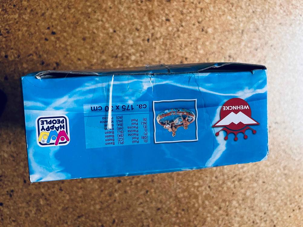 Im Test: Ein verpackter aufblasbarer Pool steht auf der Seite auf einem Holzboden.
