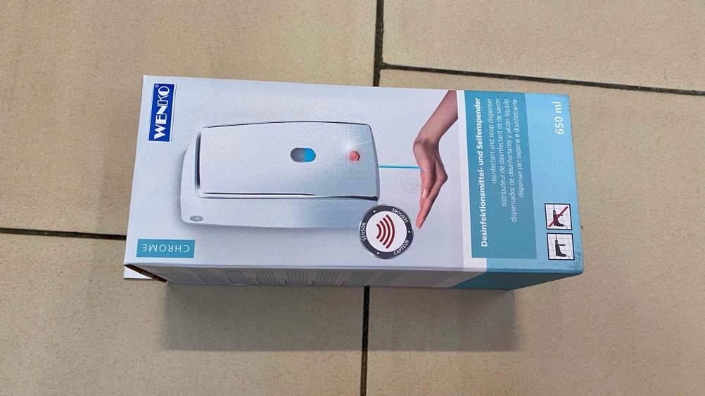 Seifenspender (Wand) getestet: Ein verpackter Spender horizontal auf einer Fließenoberfläche.