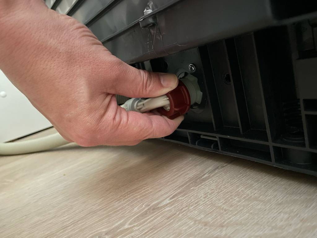 Eine Hand befestigt einen getesteten Aquastop-Schlauch an einer Waschmaschine.