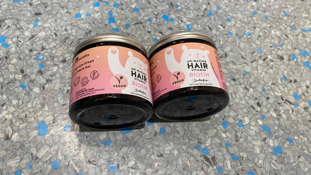 Zwei getestete Packungen Haar-Vitamine nebeneinander auf einer graublauen Oberläche