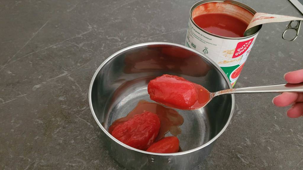 Dosentomaten im Test: eine Dosentomate auf einem Löffel und zwei weitere in einer Schüssel, die sich neben der Dose befindet.