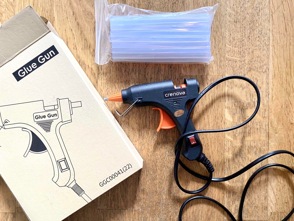 Heißklebepistole mit Klebesticks und Verpackung auf einem Holztisch