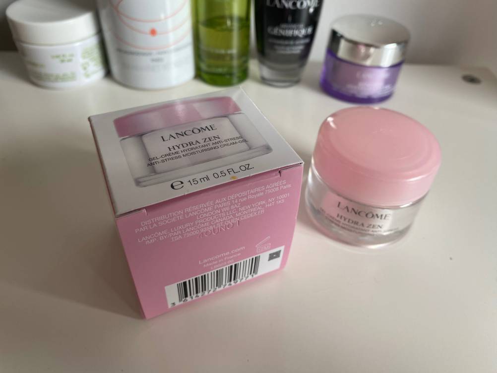 Creme und dessen Verpackung auf einem Tisch mit einigen Pflegeprodukten im Hintergrund.
