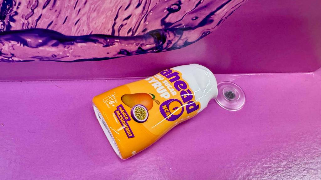 Getesteter Sirup ohne Zucker in der Sorte Mango liegt auf einer lilafarbigen Fläche.