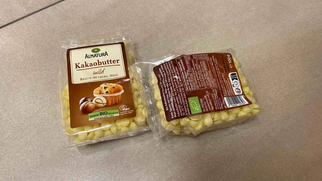 Kakaobutter im Test: zwei Packungen Kakaobutter liegend - bei einer die Vorder- und bei anderen die Rückseite ersichtlich.