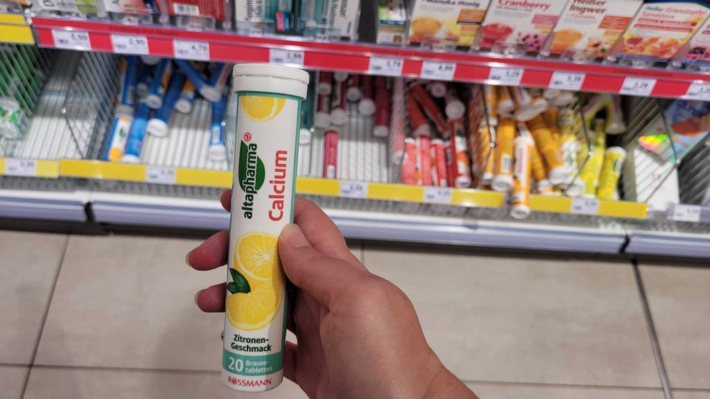 Calcium-Brausetablette im Test: Calcium-Brausetablette mit Zitronengeschmack wird vor einem Regal in der Hand gehalten.