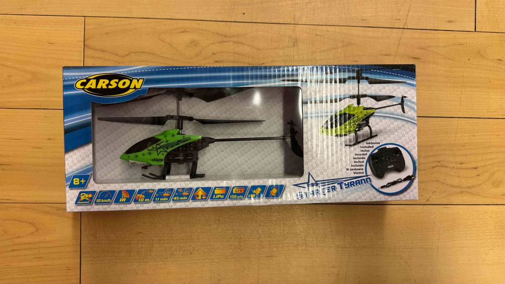 Der getestete ferngesteuerte Hubschrauber in der Farbe Grün, Schwarz ist in der Verpackung auf dem Boden platziert.