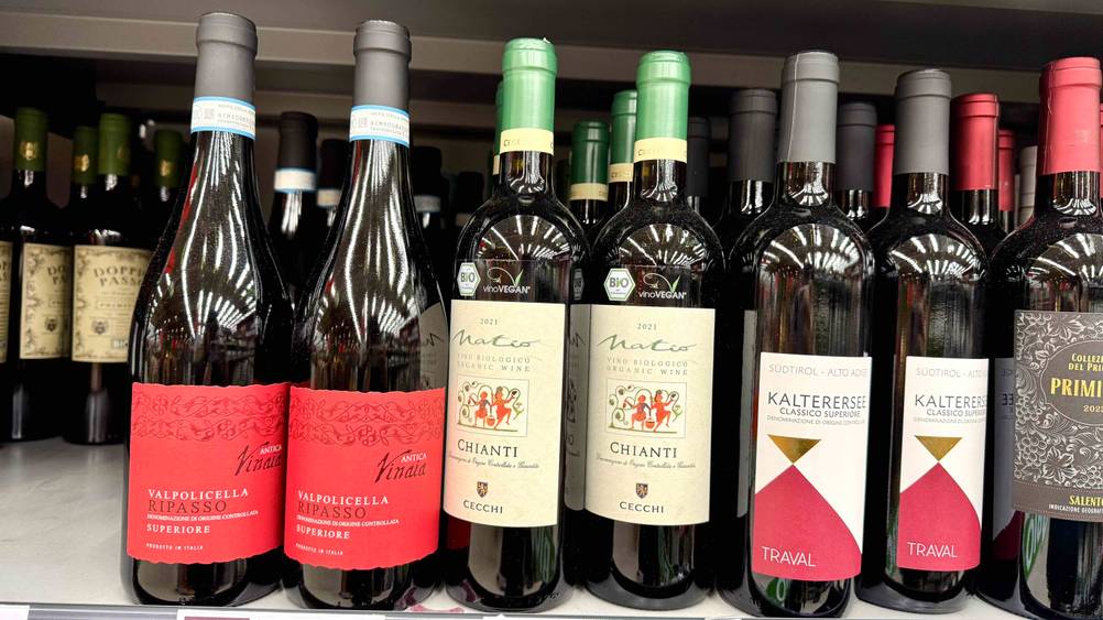Mehrere getestete Flaschen Chianti stehen neben anderen alkoholischen Getränken in einem Regal.