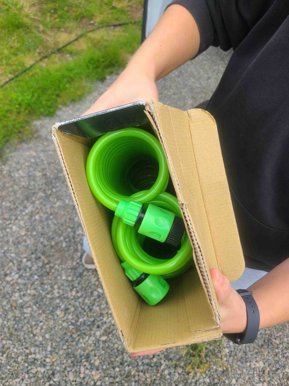 Die geöffnete Verpackung des getesteten Spiral-Gartenschlauchs wird in der Hand gehalten, während der Inhalt ersichtlich ist.