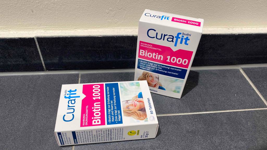 Biotin im Test: Zwei Packungen Biotin eine stehend, eine liegend auf einem grauen Boden