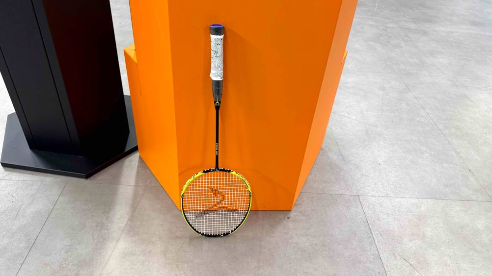 Der getestete Badmintonschläger für Kinder lehnt vertikal an einer Zwischenwand.