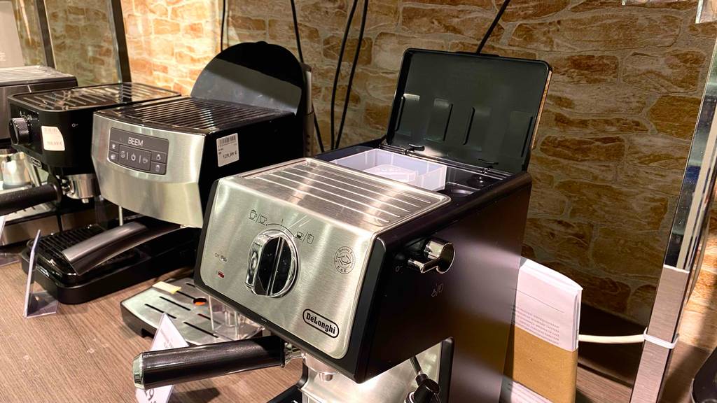 De’Longhi Siebträger-Maschine-Test: eine De’Longhi Siebträger-Maschine mit geöffnetem Wassertankfach ist in einem Geschäft neben anderen Modellen ausgestellt,