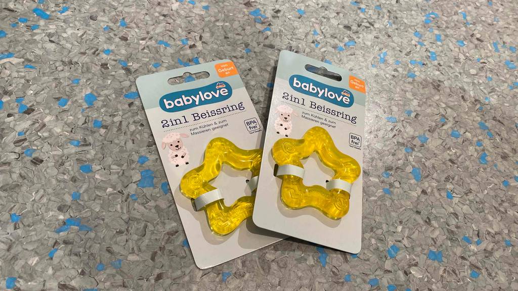 Beißring-Test: Zwei gelbe, sternförmige Beißringe in ihrer Verpackung auf grauem Untergrund. 