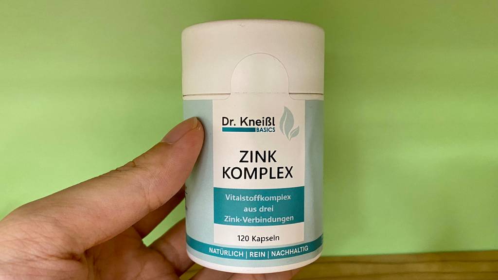 Zink getestet: Verpackung von Zink-Komplex in der Hand vor grüner Wand.