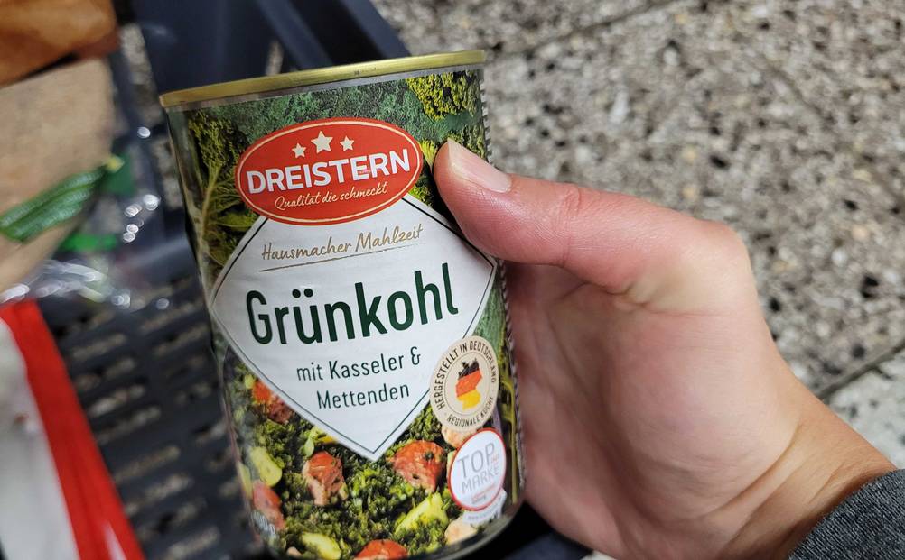 Im Test: Eine Hand hält eine Dose Gruenkohl vor einen Fließenboden