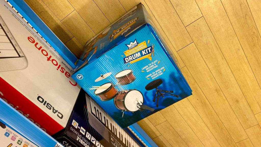 Im Test: Vor einem Regal liegt ein verpacktes Kinderschlagzeug.