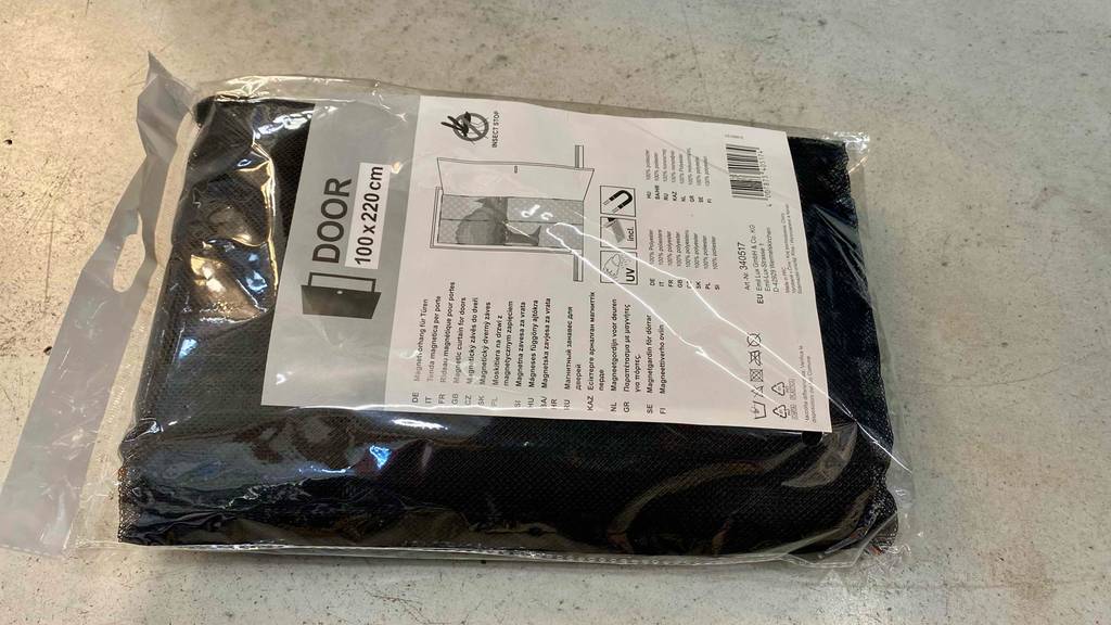 Fliegengittertüre getestet: eine schwarze Fliegengittertüre liegt in einer Plastikverpackung auf einem Boden.