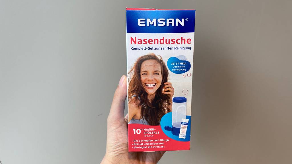 Nasendusche im Test: Eine Hand hält eine Packung Nasendusche vor eine graue Wand