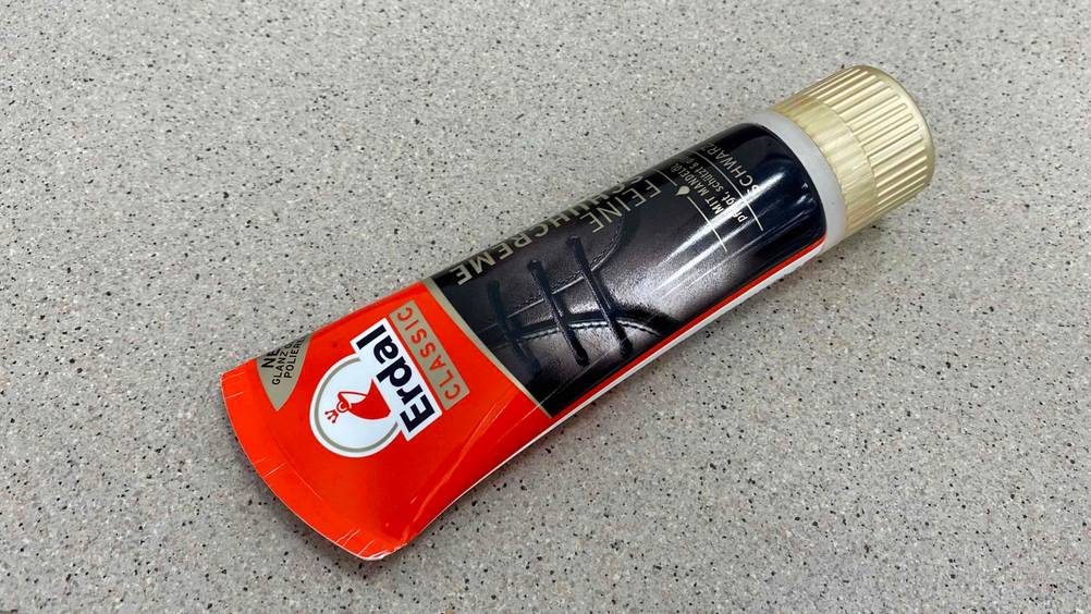 Schuhcreme im Test: Eine Tube liegt mit der Vorderseite nach oben auf einer grauen Fläche