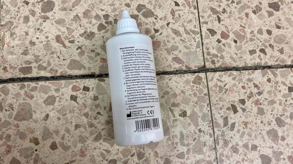 Kontaktlinsen-Pflegemittel im Test: eine Flasche Kontaktlinsen-Pflegemittel auf der Rückseite liegend auf einem Boden.