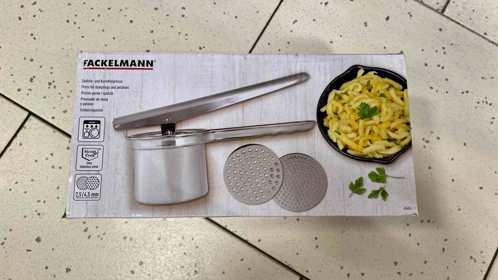 Spätzepresse im Test: Verpackung von Spätzepresse der Marke Fackelmann mit verschiedenen Aufsätzen liegt auf einem Boden.