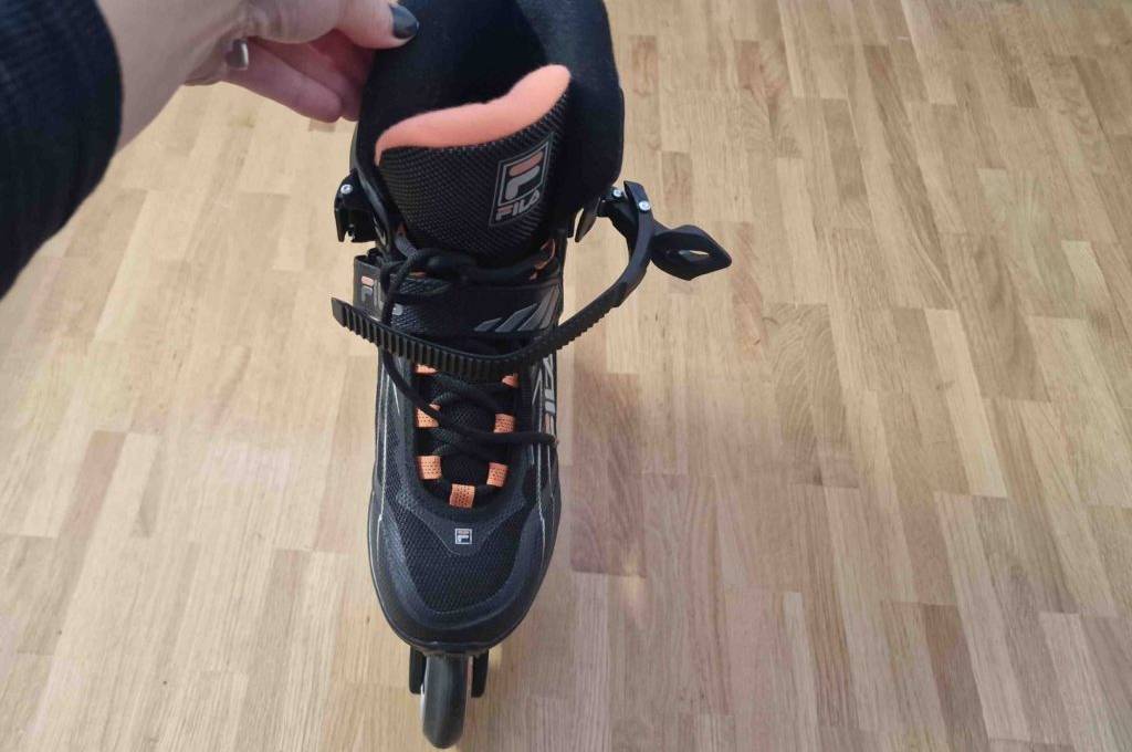 Eine Hand hält einen getesteten Inline-Skate für Damen aufrecht auf einem Holzboden.