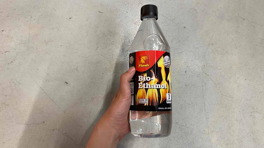 Bioethanol getestet: Eine Hand hält eine Flasche vor einen Steinboden