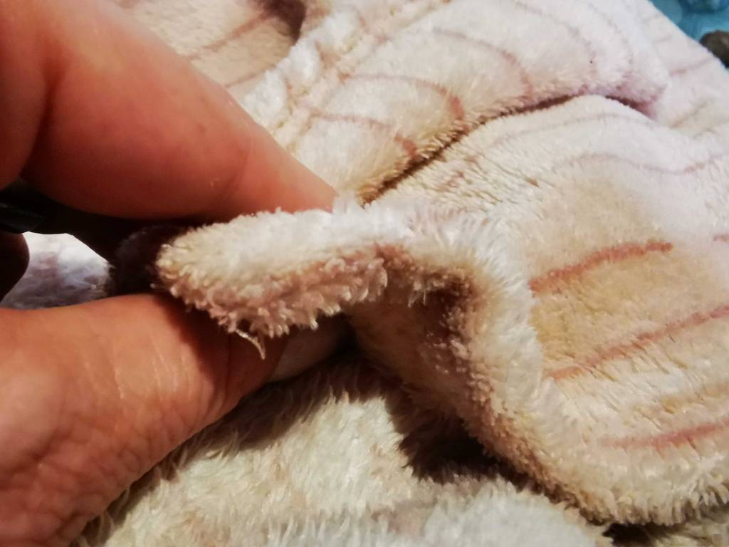 Zwei Finger befühlen das Material der rosa Fleecedecke im Test.