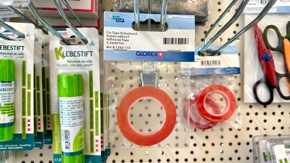 Das getestete Klebeband hängt in einem Regal neben Klebestifen.